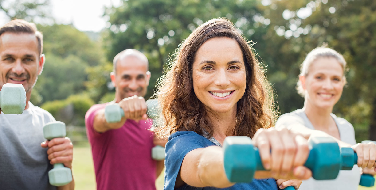 Eine Gruppe Erwachsener trainiert im Freien mit kleinen Hanteln