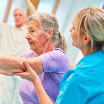 Seniorin wird von einer Trainerin bei einer bung angeleitet
