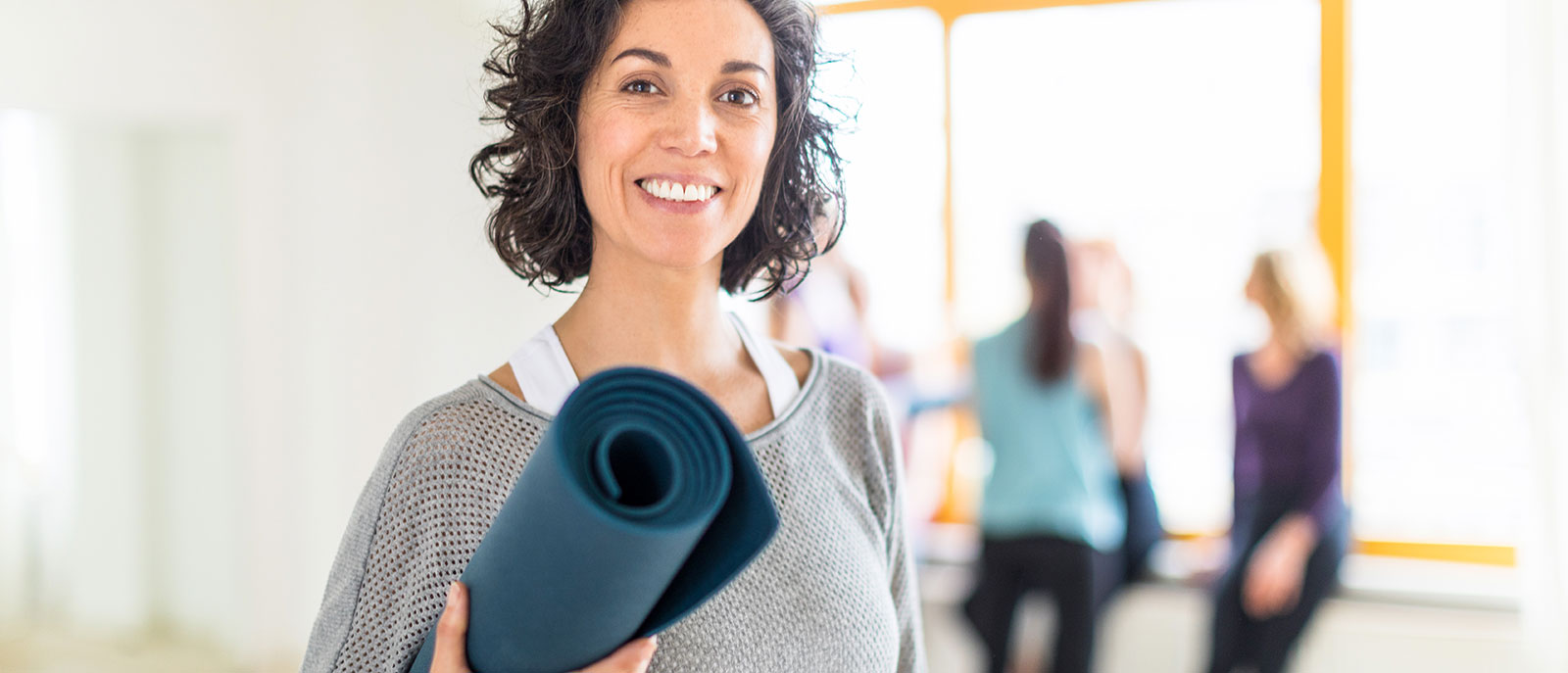 Halbportrt eine Frau mit Trainingsmatte lchelt in die Kamera
